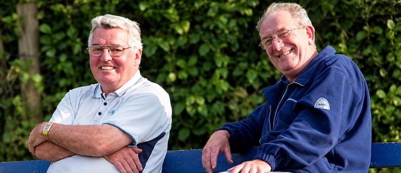 Two friends smiling at the cricket ground, from the photographs shared in memory of Reg Hargan